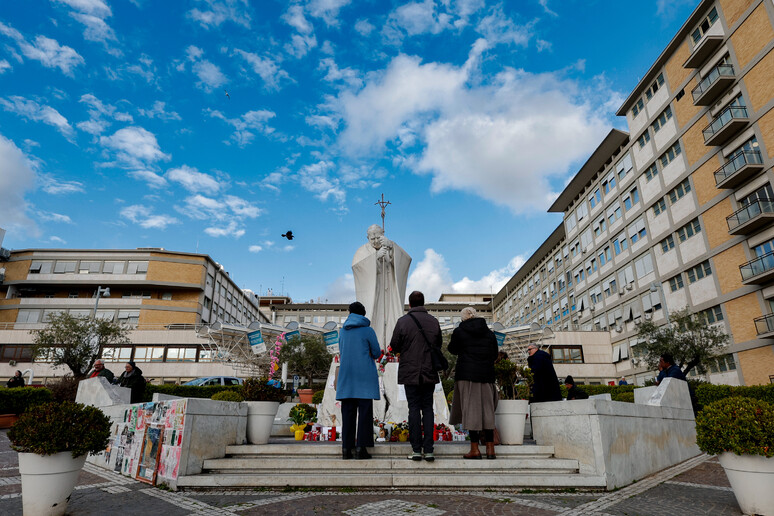 People pray under the statue of late Pope John Paul II outside Agostino Gemelli - RIPRODUZIONE RISERVATA